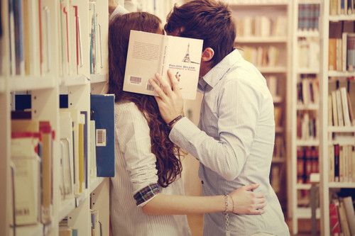 Couple kissing in a library behind a book