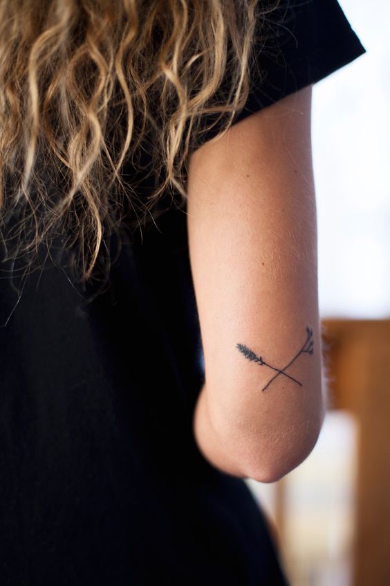 small crossed arrows tattoo on back of arm